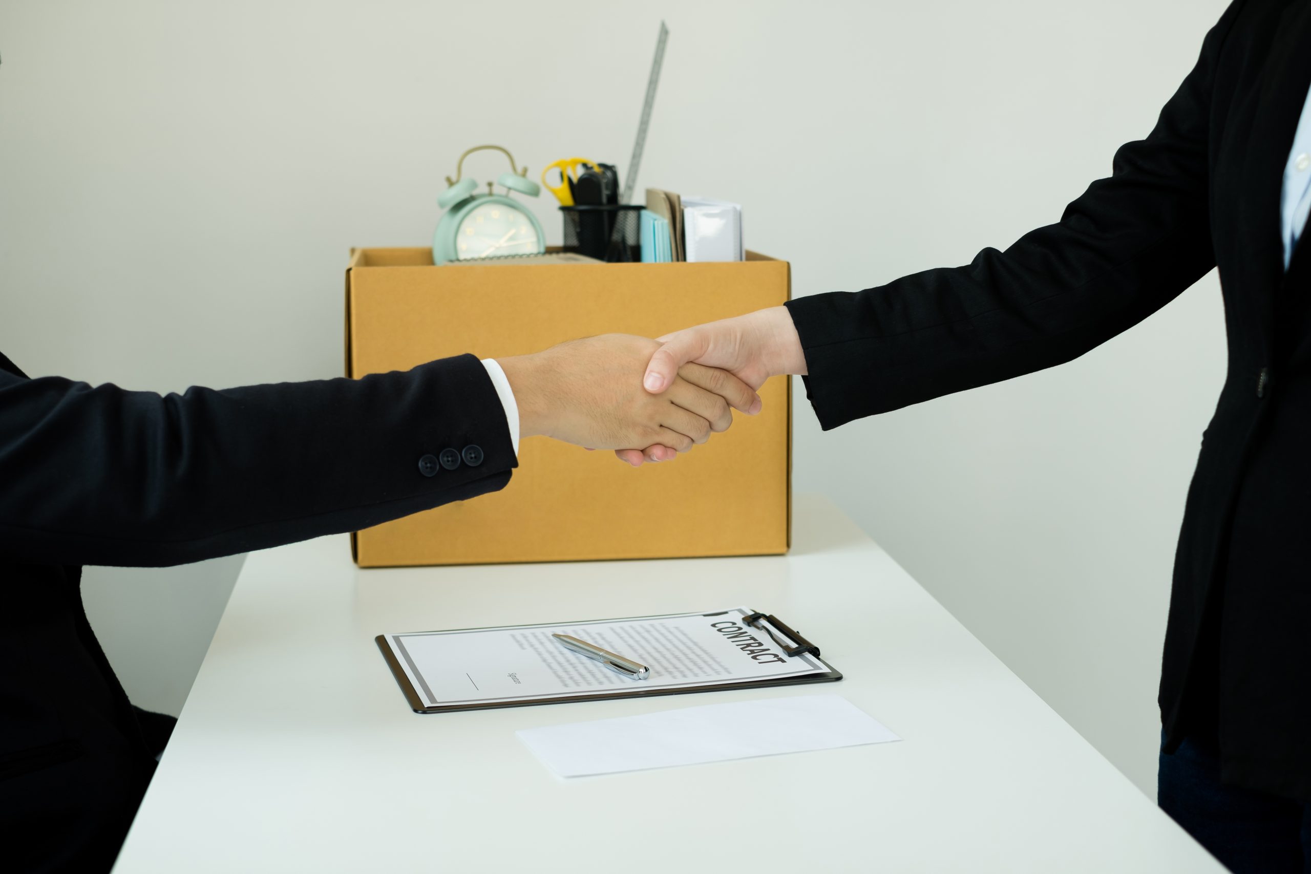 Desperately fired female office worker employee hands her employer her resignation letter, packs her belongings in a cardboard box, and shaking hands with boss concept dismissal and unemployment.
