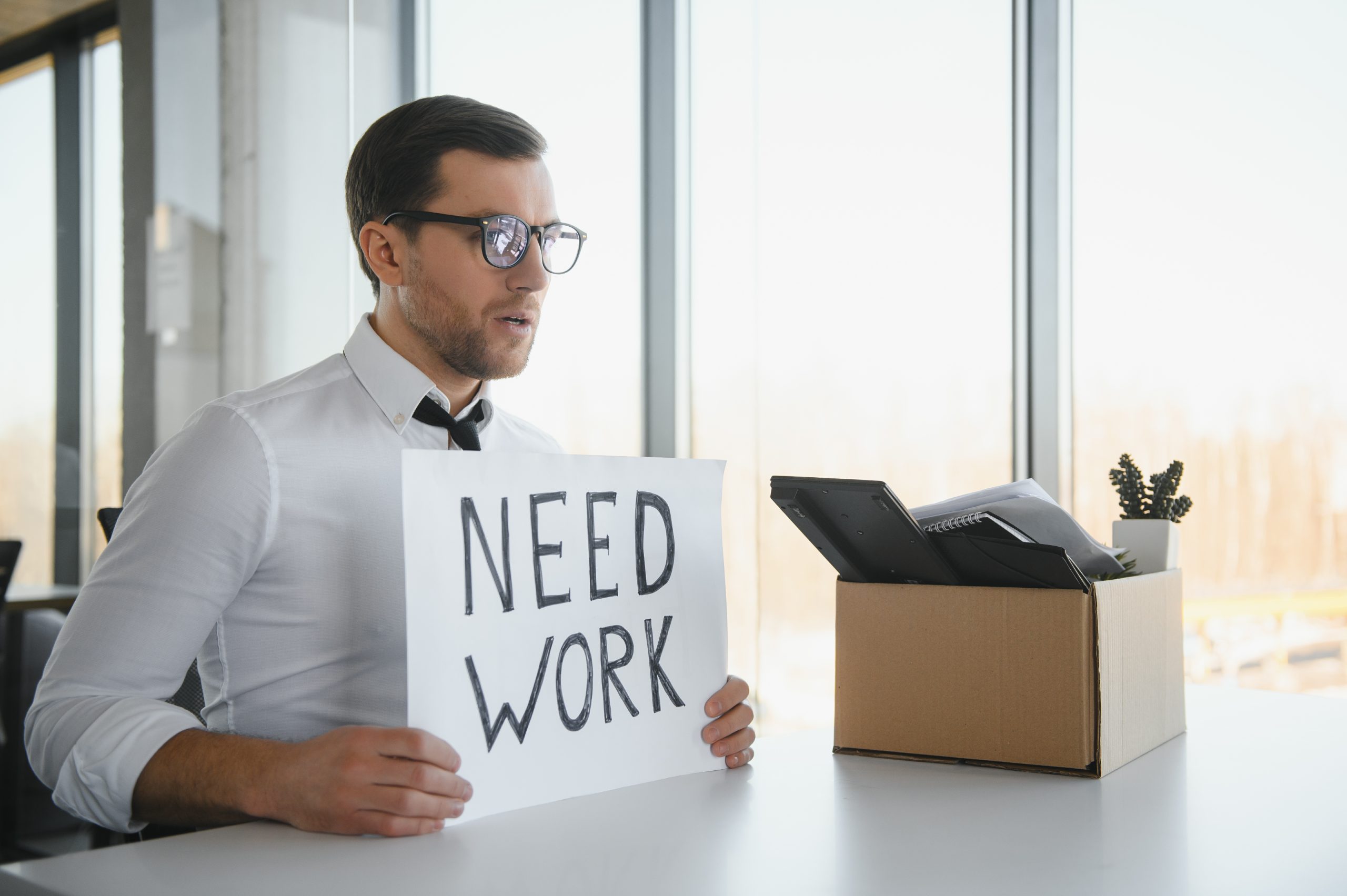 Man sitting with a need work poster